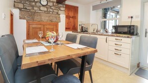 A kitchen with a stone wall, wooden cabinets, a microwave, and a dining area with chairs and a table set for two. - 2 The Square (Skipton)