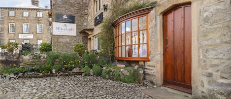 A cobbled courtyard with a stone building featuring a wooden door and a window with a grid pattern.
