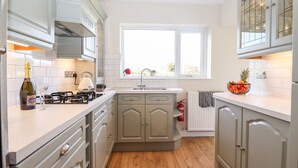 Une cuisine moderne avec des meubles gris, un plan de travail blanc, une cuisinière à gaz et une fenêtre donnant sur un paysage verdoyant.