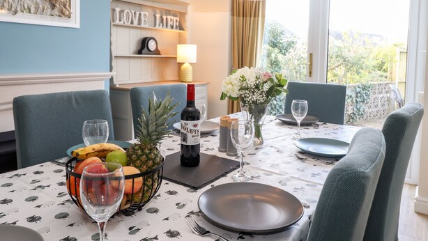 Une table à manger dressée avec des assiettes, des verres, une bouteille de vin et un panier de fruits.