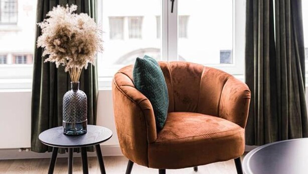 A room with a brown armchair, a small round table with a vase of dried flowers, and a blue rug. - Gorgeous Apartment in old City Centre of Antwerp 1 (Antwerp)
