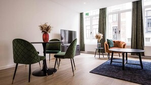 A modern living room with a TV, two green chairs, a round table, and a sofa. - Gorgeous Apartment in old City Centre of Antwerp 1 (Antwerp)