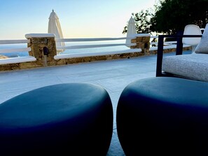 Une terrasse avec un mur en pierre, un bâtiment blanc en arrière-plan et une vue sur la mer.
