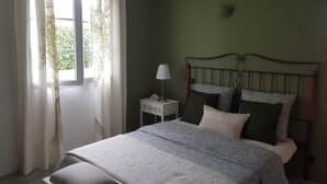 A bedroom with a bed, curtains, a bedside lamp, and a nightstand. - The villa (Beauvoisin)
