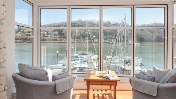 A room with two grey sofas facing a large window overlooking a marina with boats. - 33 Dart Marina (Dartmouth)