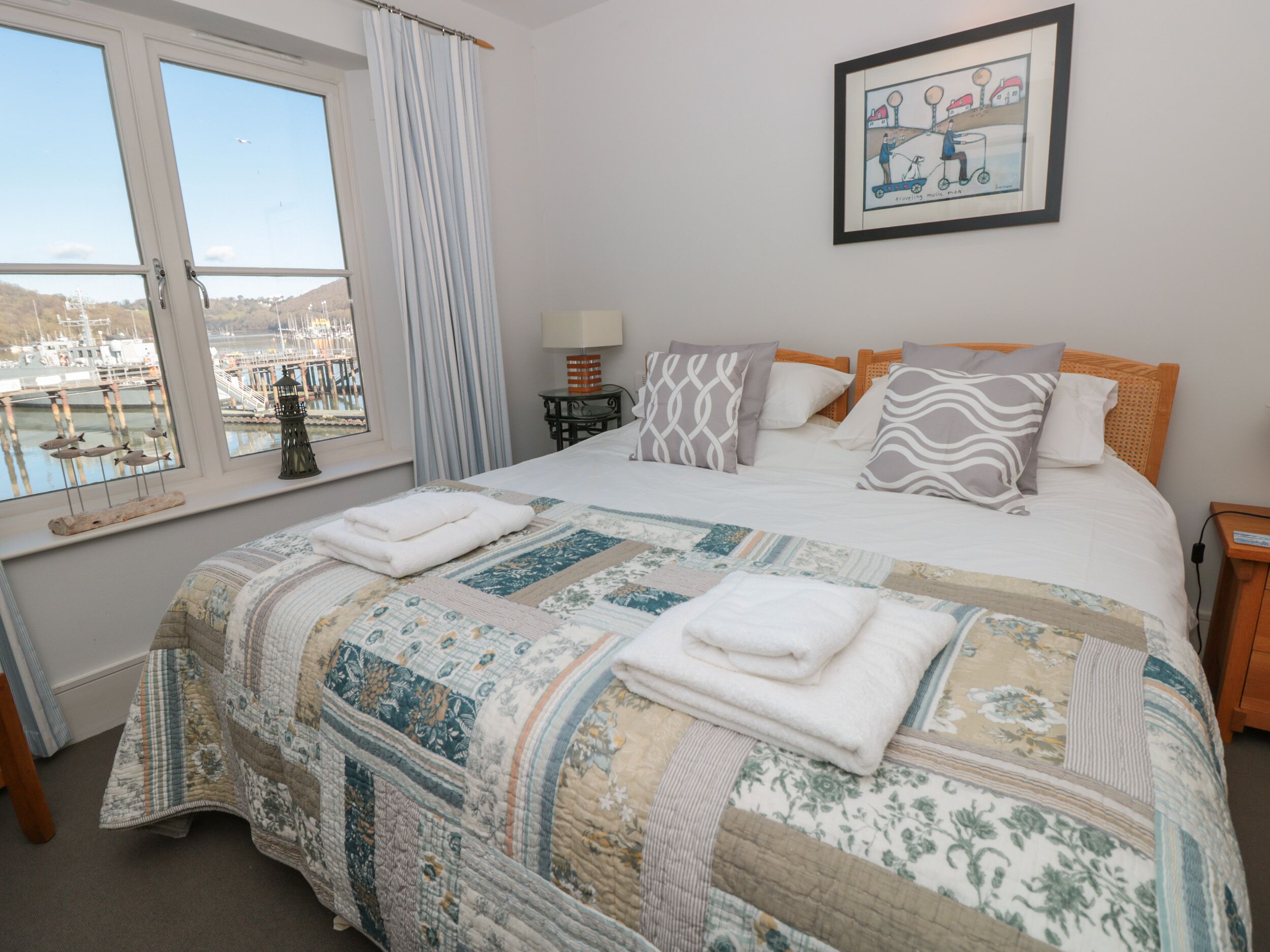 Un dormitorio con una cama grande, una ventana con vista a barcos y un cuadro en la pared.