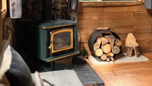 A cozy cabin interior with a wood-burning stove, stone wall, and a window with curtains. - Romantic Off-Grid Cabin (Lytton)