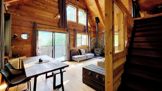 A log cabin interior with a dining area, sofa, fireplace, and a staircase. - Romantic Off-Grid Cabin (Lytton)