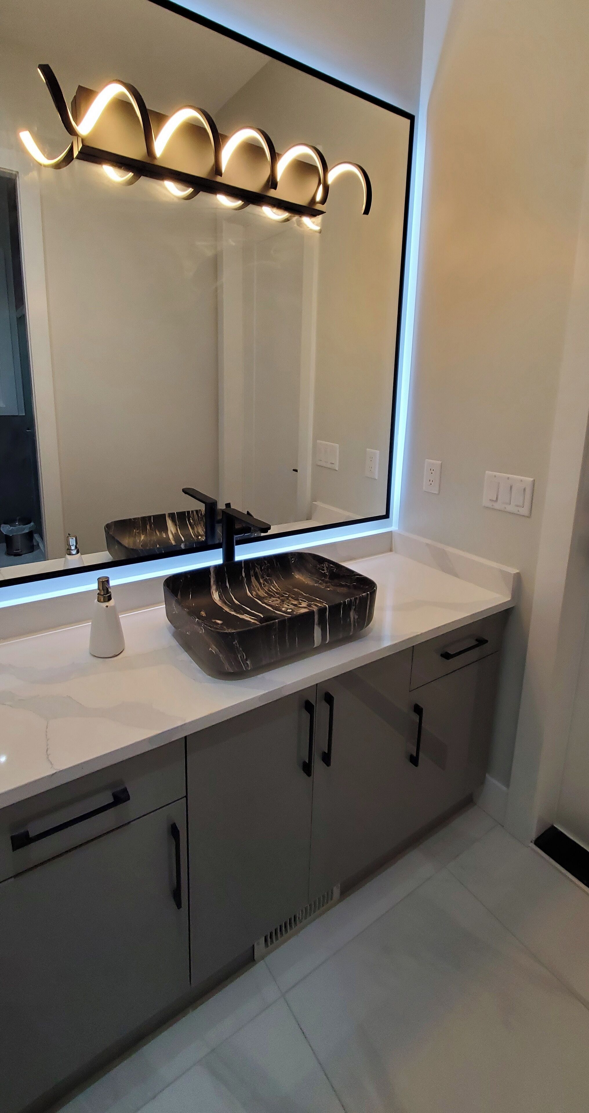 A modern bathroom with a large mirror, a black marble sink, and a sleek vanity.