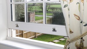 A window with a view of a garden, a brick wall, and a wooden fence. - Acorn Cottage (Driffield)