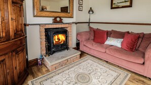 A living room with a brick fireplace, a pink sofa, a wooden cabinet, and a large mirror on the wall. - Acorn Cottage (Driffield)