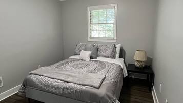 Un dormitorio con cama, mesita de noche, lámpara y ventana.