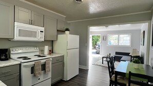 Une cuisine compacte équipée d’une cuisinière, d’un four à micro-ondes et d’un réfrigérateur. Un coin repas avec une table et des chaises est également disponible.