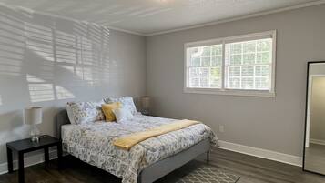 Un dormitorio con cama, mesita de noche, lámpara, ventana y espejo.