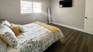 Une chambre à coucher avec un lit, une fenêtre, un téléviseur à écran plat et une porte.