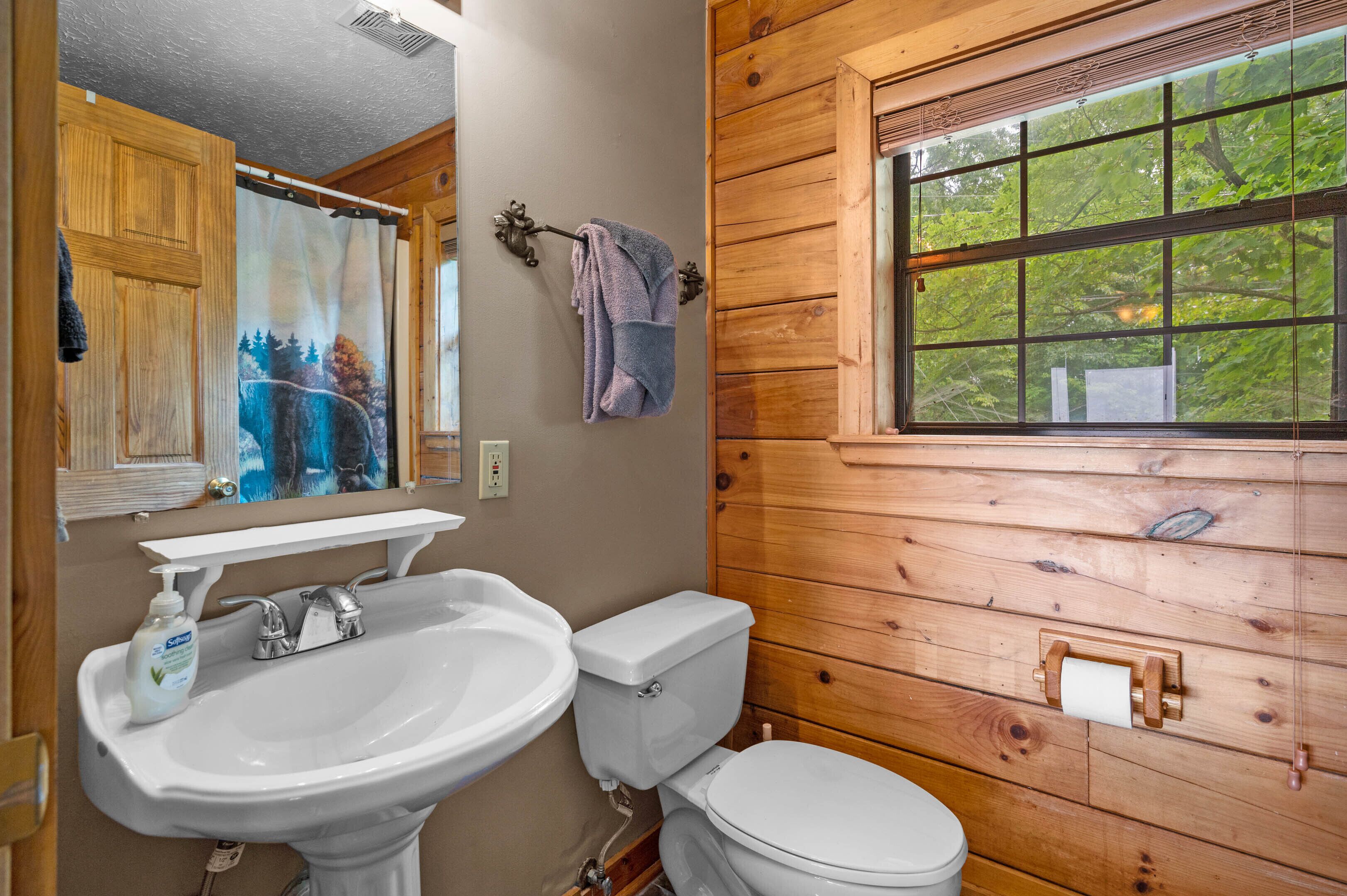 Une salle de bain avec un mur en bois, une fenêtre donnant sur des arbres, un lavabo et des toilettes.