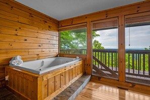 A wooden cabin with a large wooden bathtub, a balcony with a railing, and a view of trees and sky. - Semi-secluded Family Cabin w/ Sunset Views near Pigeon Forge! Games and Hot Tub! (Sevierville)