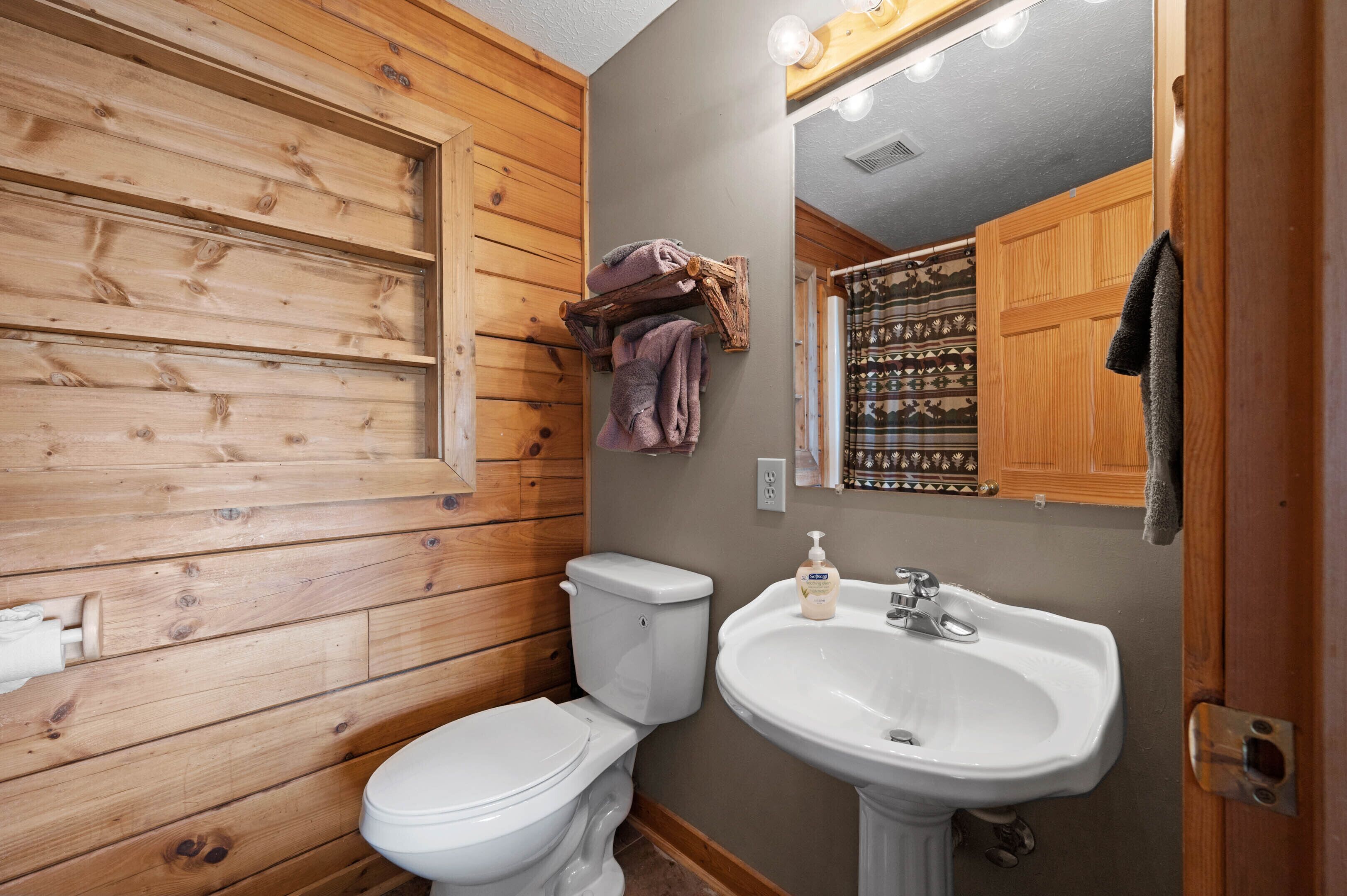 Een badkamer met houten wanden, een wit toilet, een wastafel en een spiegel met verlichting.
