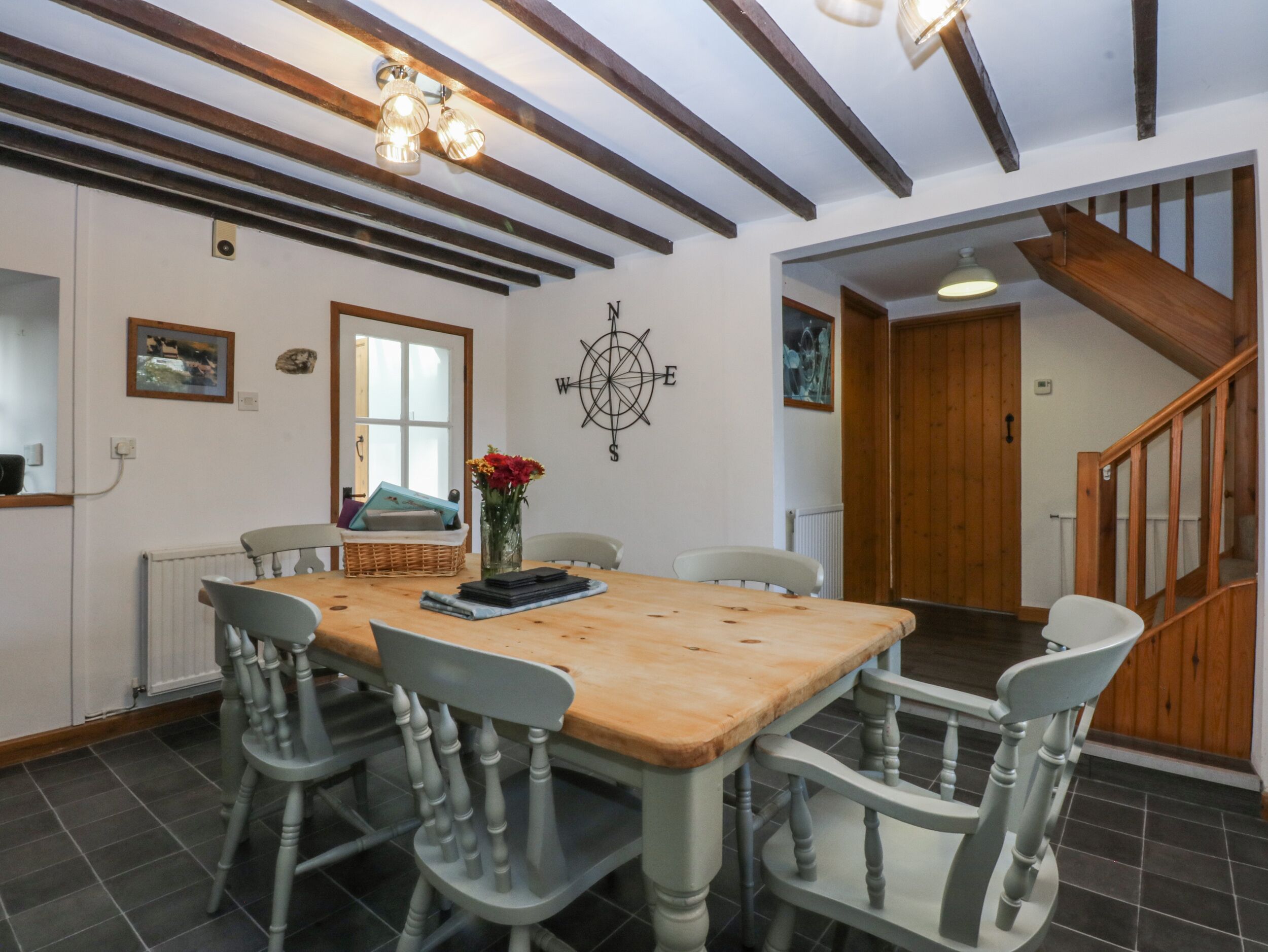A dining area with a wooden table and four chairs, a compass wall decoration, and a staircase leading to another room.