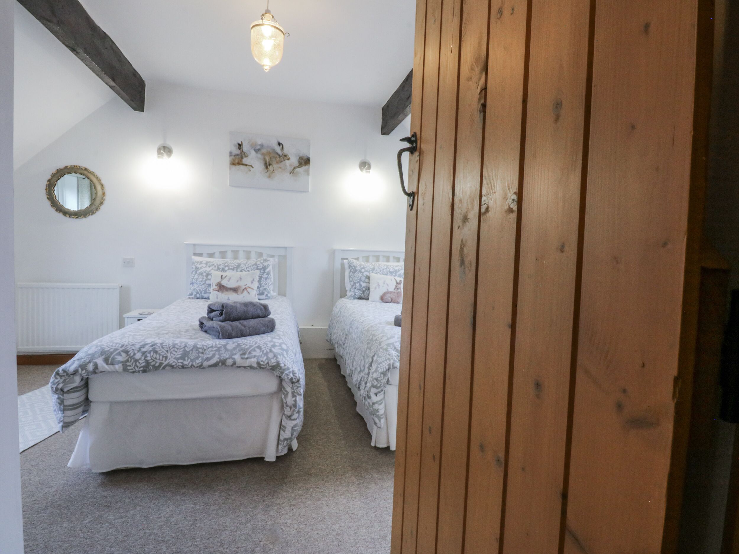 Camera da letto con due letti, una porta in legno, una lampada a soffitto, uno specchio fissato al muro e un quadro con dei cervi.