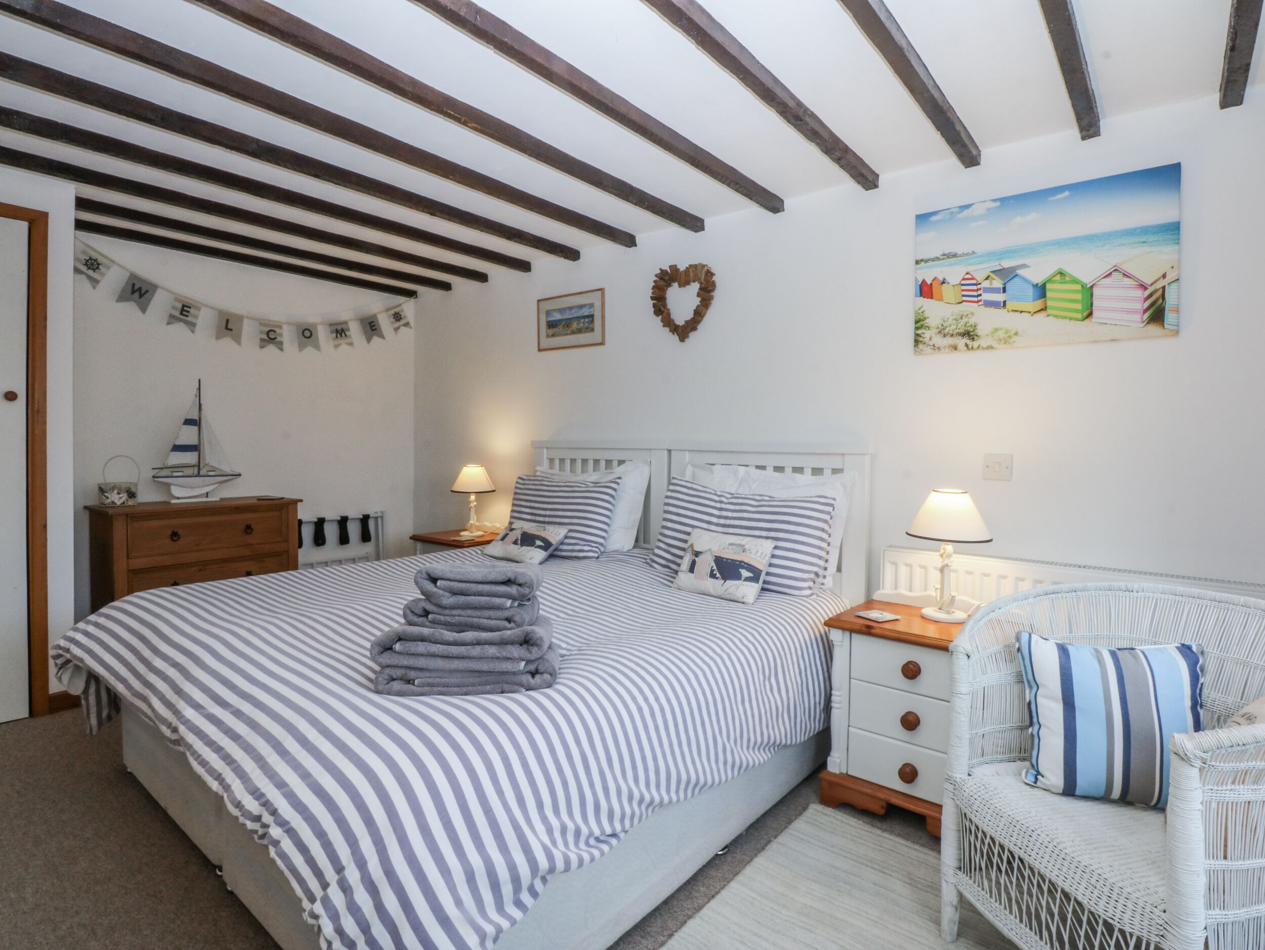A bedroom with a bed, two bedside tables, a nightstand, a wicker chair, and a wall with a picture and a heart decoration.
