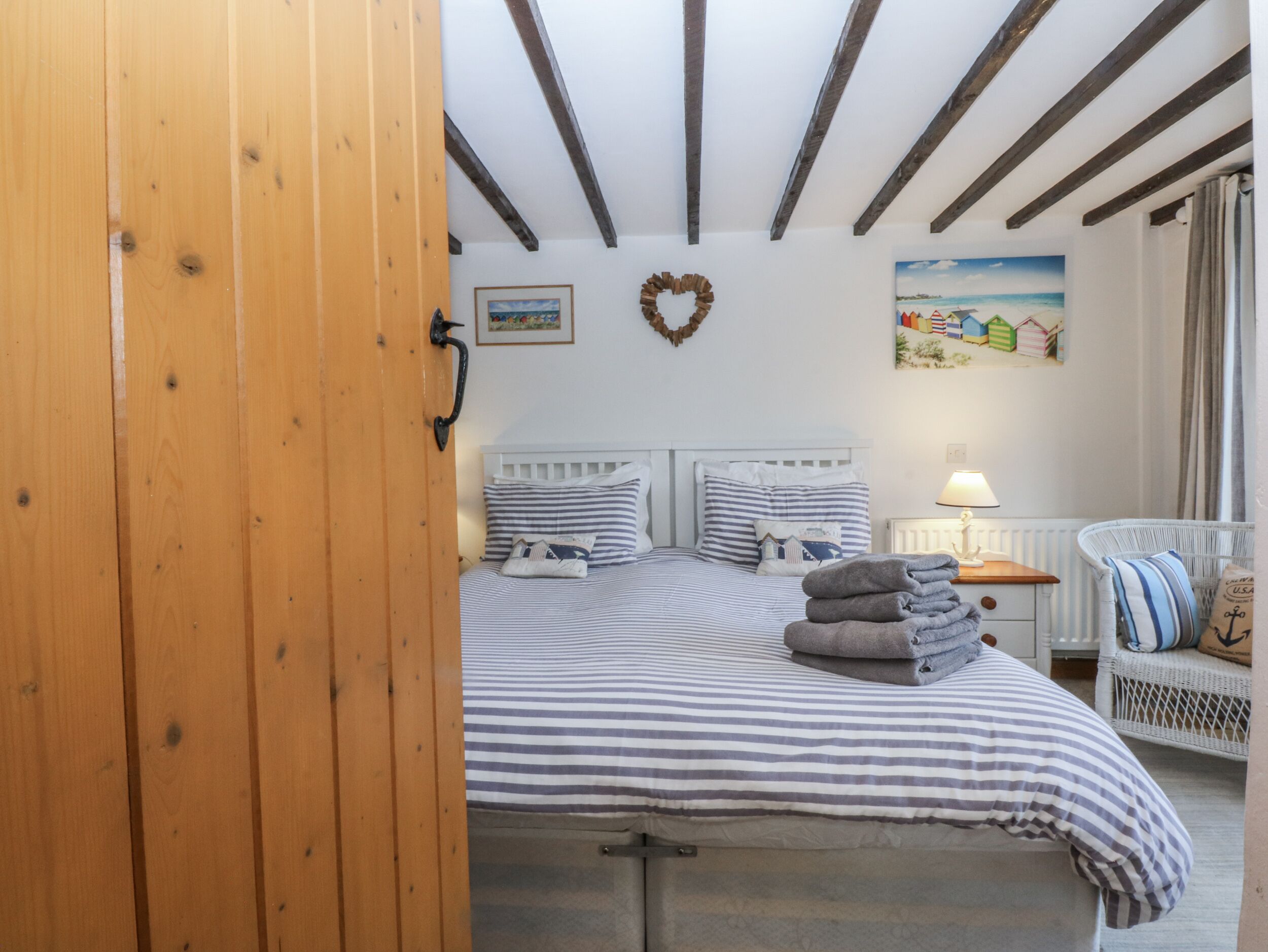 A bedroom with a bed, a nightstand, a wicker chair, and a painting on the wall.