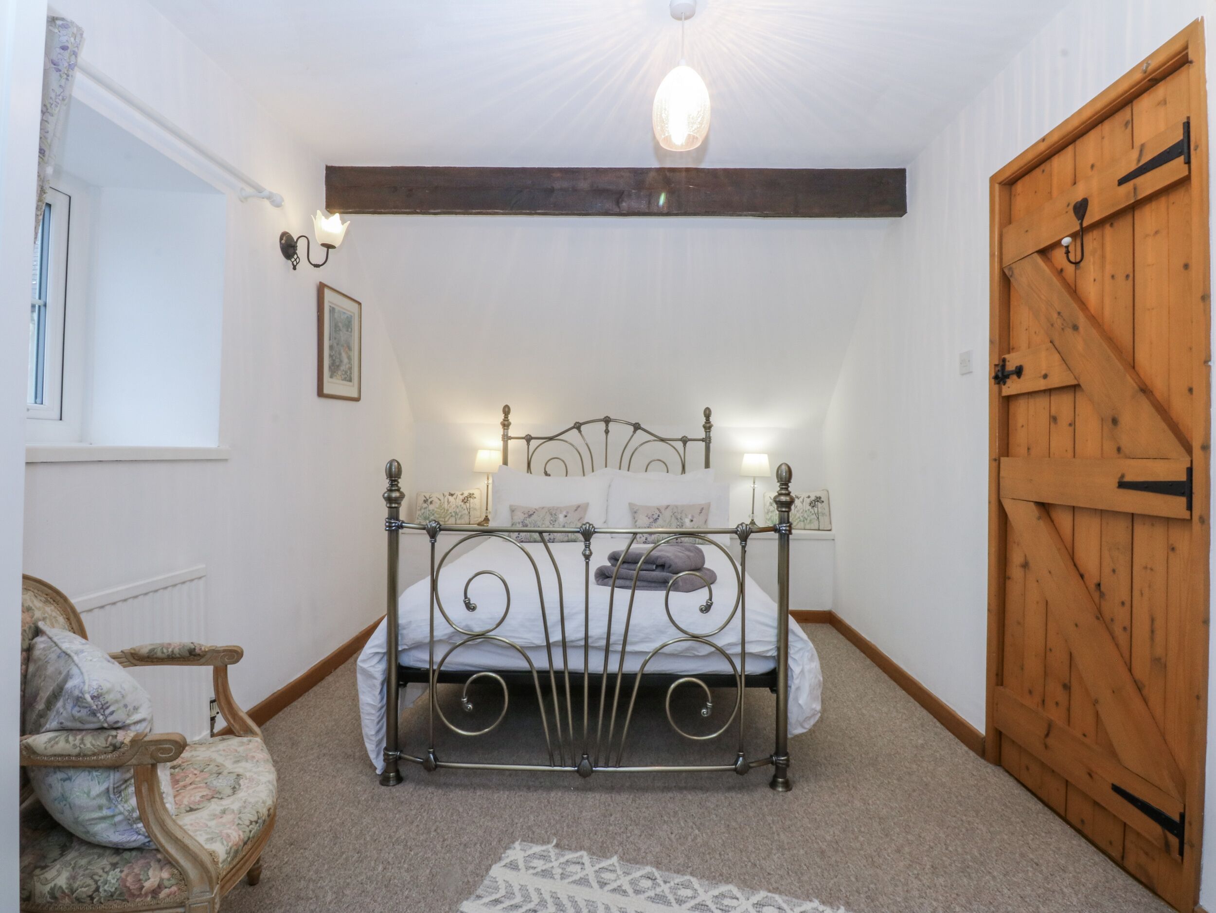 A bedroom with a metal bed frame, a wooden door, a chair, and a light fixture on the ceiling.