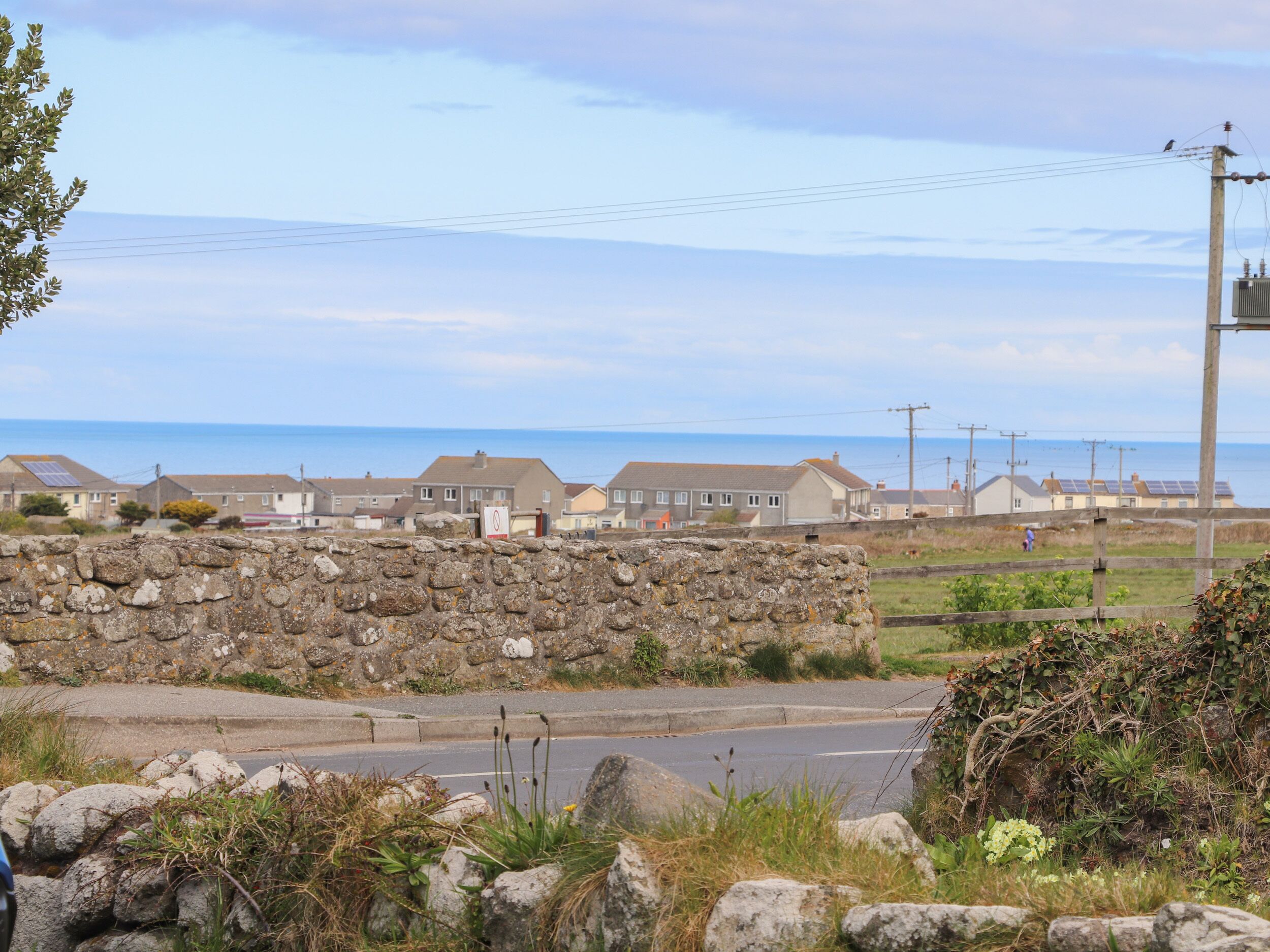 A coastal road with stone walls and houses in the background.