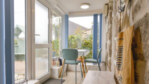 Ein Zimmer mit einem Holztisch, zwei grünen Stühlen, einer weißen Tischdecke und einem Fenster mit blauen Vorhängen.