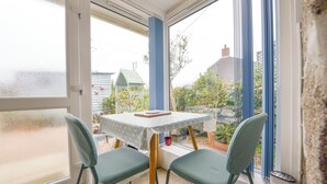 Ein Wintergarten mit Tisch und zwei Stühlen, Blick auf den Garten, und ein blauer Stuhl, der an die Wand gelehnt ist.