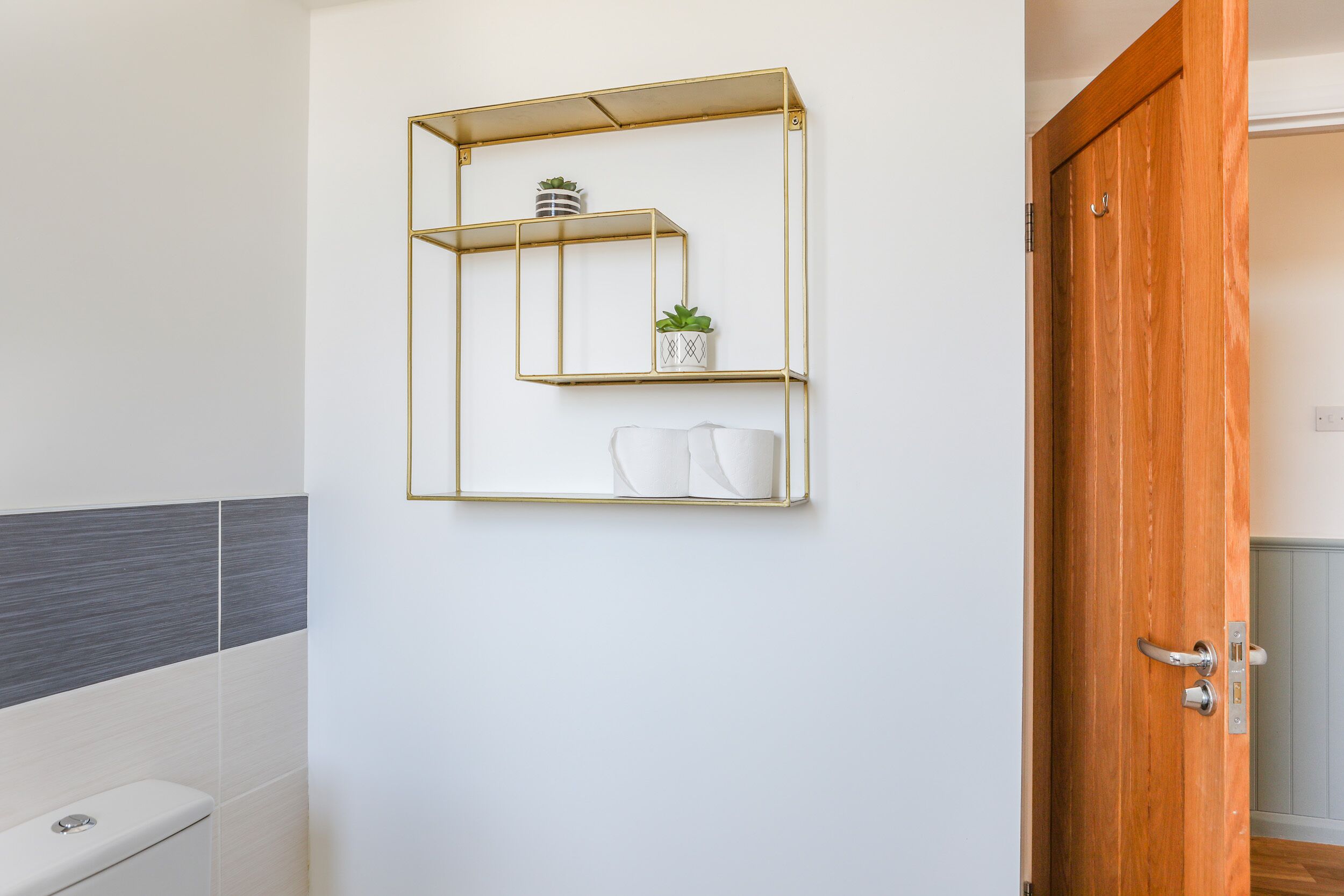 Une salle de bain avec des toilettes blanches, un mur recouvert de carreaux gris et blancs, et une porte en bois.