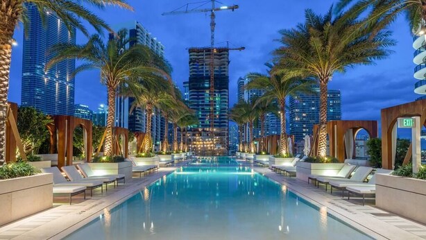 A swimming pool with lounge chairs and palm trees, surrounded by high-rise buildings. - Suite 212 located in SLS Lux Brickell by City Escapes (Miami)