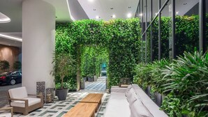 A modern indoor lobby with a geometric patterned floor, a white sofa, wooden tables, and a green vertical garden wall. - Suite 212 located in SLS Lux Brickell by City Escapes (Miami)