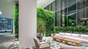 An indoor seating area with a sofa, chairs, and a coffee table, surrounded by lush green plants and a patterned floor. - Suite 212 located in SLS Lux Brickell by City Escapes (Miami)
