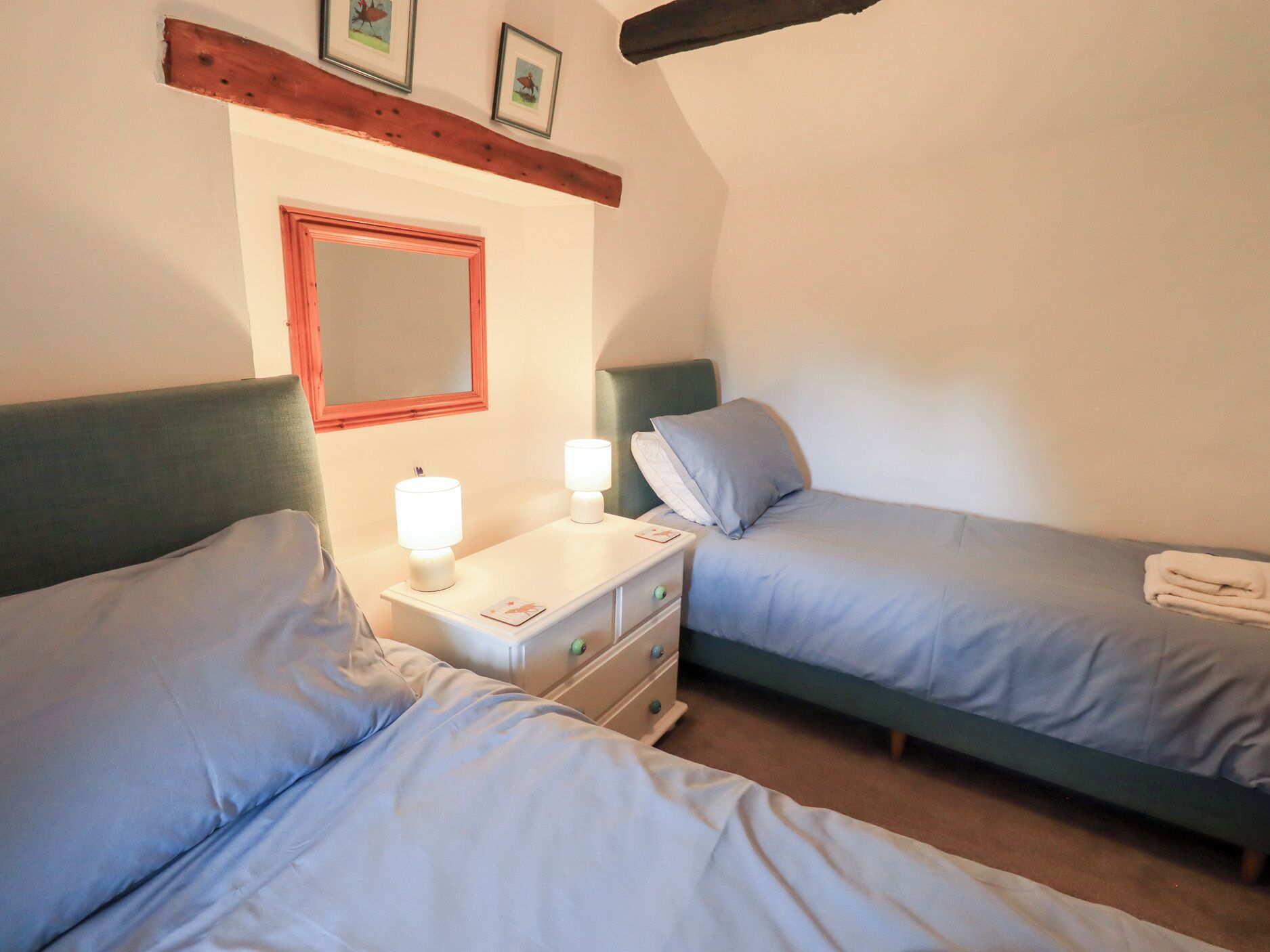 Una habitación con dos camas individuales, una mesita de noche con lámpara, un espejo y una viga de madera sobre las camas.