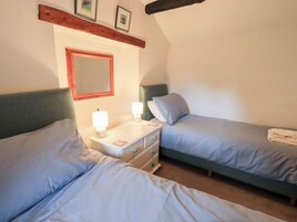 Una habitación con dos camas individuales, una mesita de noche con lámpara, un espejo y una viga de madera sobre las camas.