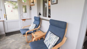 Un porche con dos sillones tapizados en azul, una pequeña mesa de madera y una lámpara de pared.
