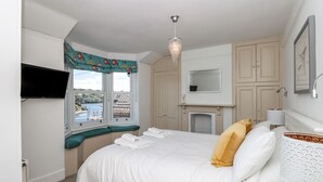 Ein Schlafzimmer mit Bett, Fernseher, Fenster mit Blick auf ein Gewässer und Kamin.