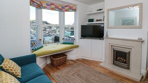 Ein modernes Wohnzimmer mit großem Fenster, Kamin, Fernseher und einer Couch.