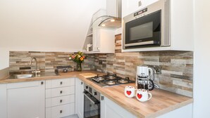 A modern kitchen with white cabinets, a wooden countertop, a gas stove, a microwave, and a coffee maker. - Woodland View (Richmond)