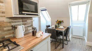 A modern kitchen with a built-in microwave, kettle, and coffee maker. There is a dining area with a table and chairs, and a window with a view of the sky. - Woodland View (Richmond)
