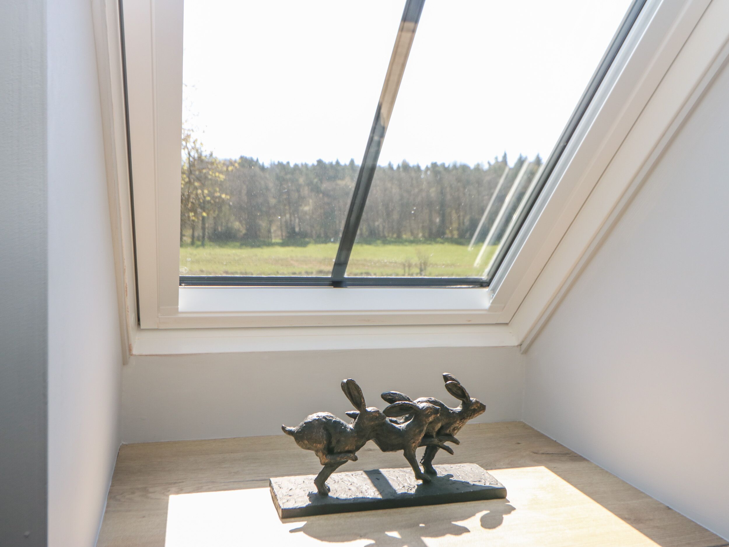 Une lucarne donnant sur une forêt et une sculpture représentant deux animaux, le tout posé sur une surface en bois.