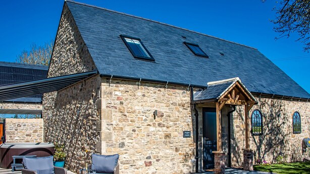 A stone building with a sloped roof, outdoor seating area, and a wooden porch. - Woodland View (Richmond)