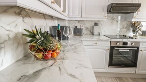 Una cucina con mobili bianchi, un piano di lavoro in marmo, una ciotola di frutta, un tostapane e un forno.