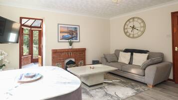 A living room with a fireplace, a grey sofa, a coffee table, and a flat-screen TV mounted on the wall.