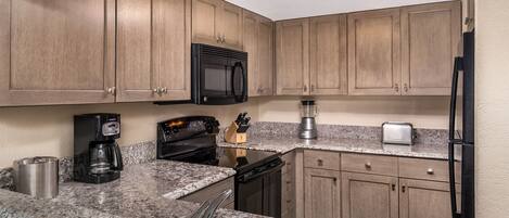 A kitchen with wooden cabinets, a black microwave, a coffee maker, a toaster, and a dishwasher.