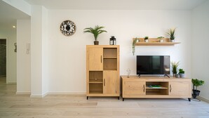 Ein Wohnzimmer mit einem Fernsehschrank aus Holz, einer Wanduhr und Regalen mit Pflanzen.