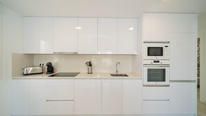 Eine moderne Küche mit weißen Schränken, einem Toaster, einer Kaffeemaschine, einer Spüle, einer Mikrowelle und einem Backofen.