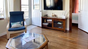 Un saló amb una poltrona blava, una taula de cafè de vidre, un televisor a la paret i un armari de fusta amb objectes decoratius.