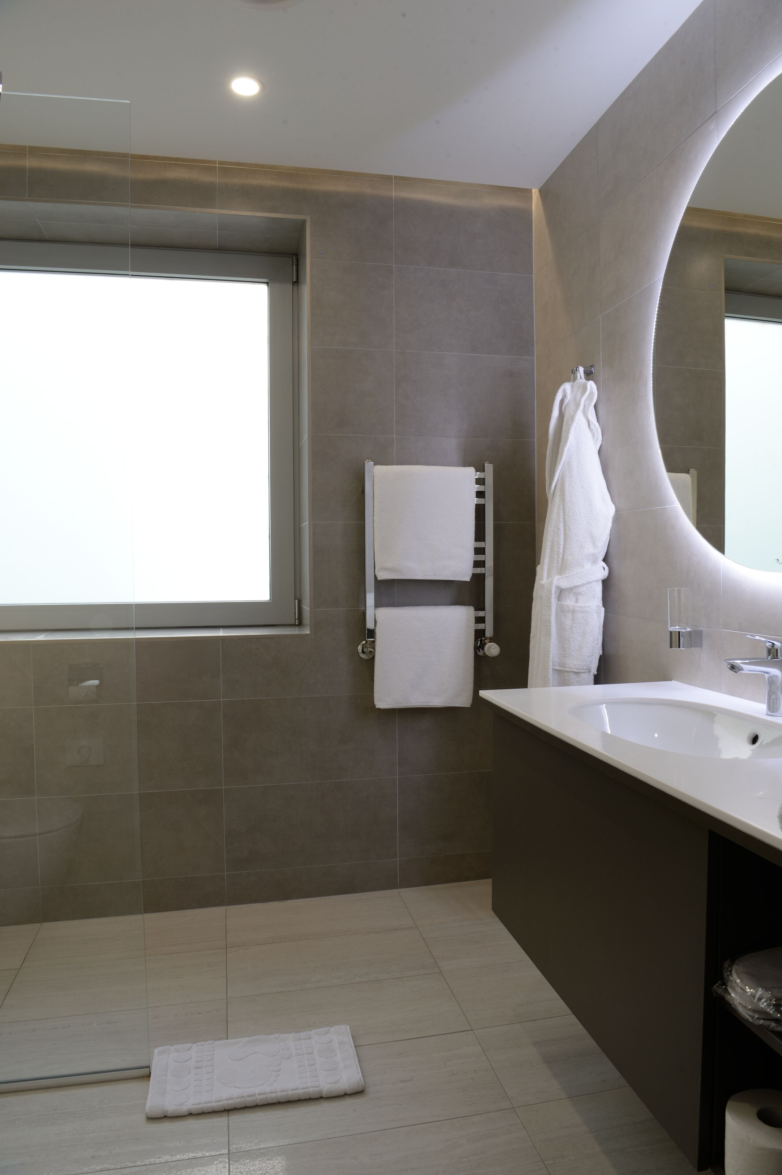 Une salle de bain moderne avec une grande fenêtre, un miroir incurvé et un lavabo blanc.